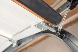 Close-up of a garage door mechanism showing a metal track, cables, and part of the door as it curves upward.